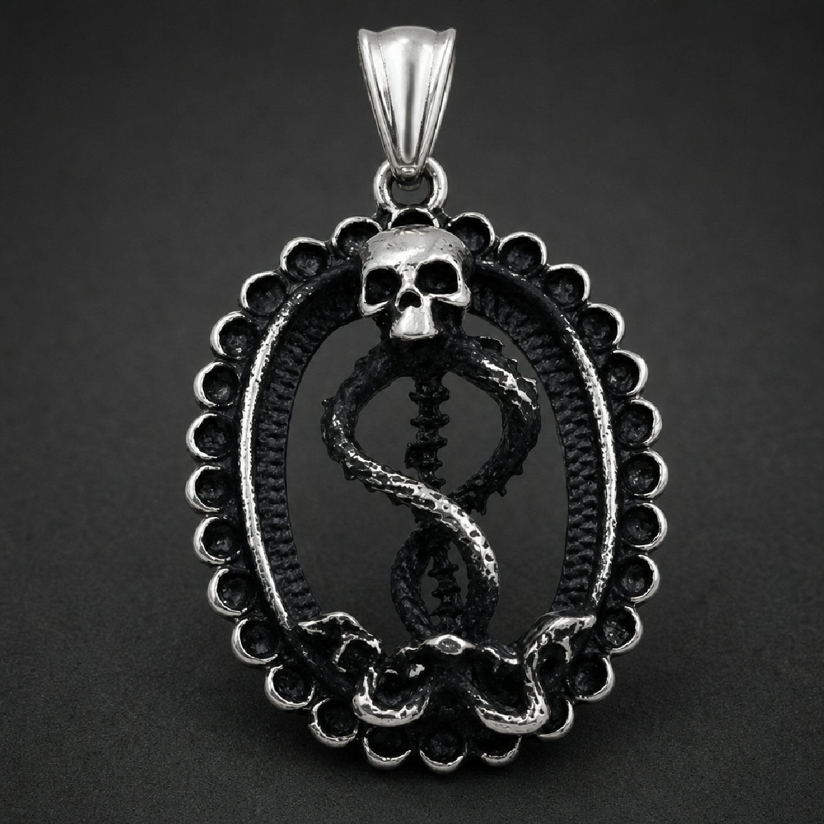 Antiqued 316L stainless steel skull and serpent pendant featuring a skull atop an entwined spinal column inside a beaded oval medallion