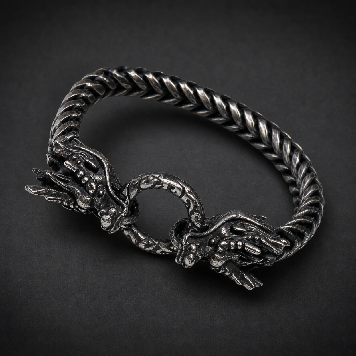 Heavy 316L stainless steel bracelet featuring two intricately detailed dragon heads clasping a ring, with a dark, antiqued finish on a woven chain.