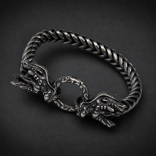 Heavy 316L stainless steel bracelet featuring two intricately detailed dragon heads clasping a ring, with a dark, antiqued finish on a woven chain.