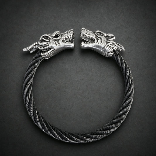 Dual snarling wolf head bracelet with a twisted dark cable band made of 316L surgical stainless steel on a wooden surface.