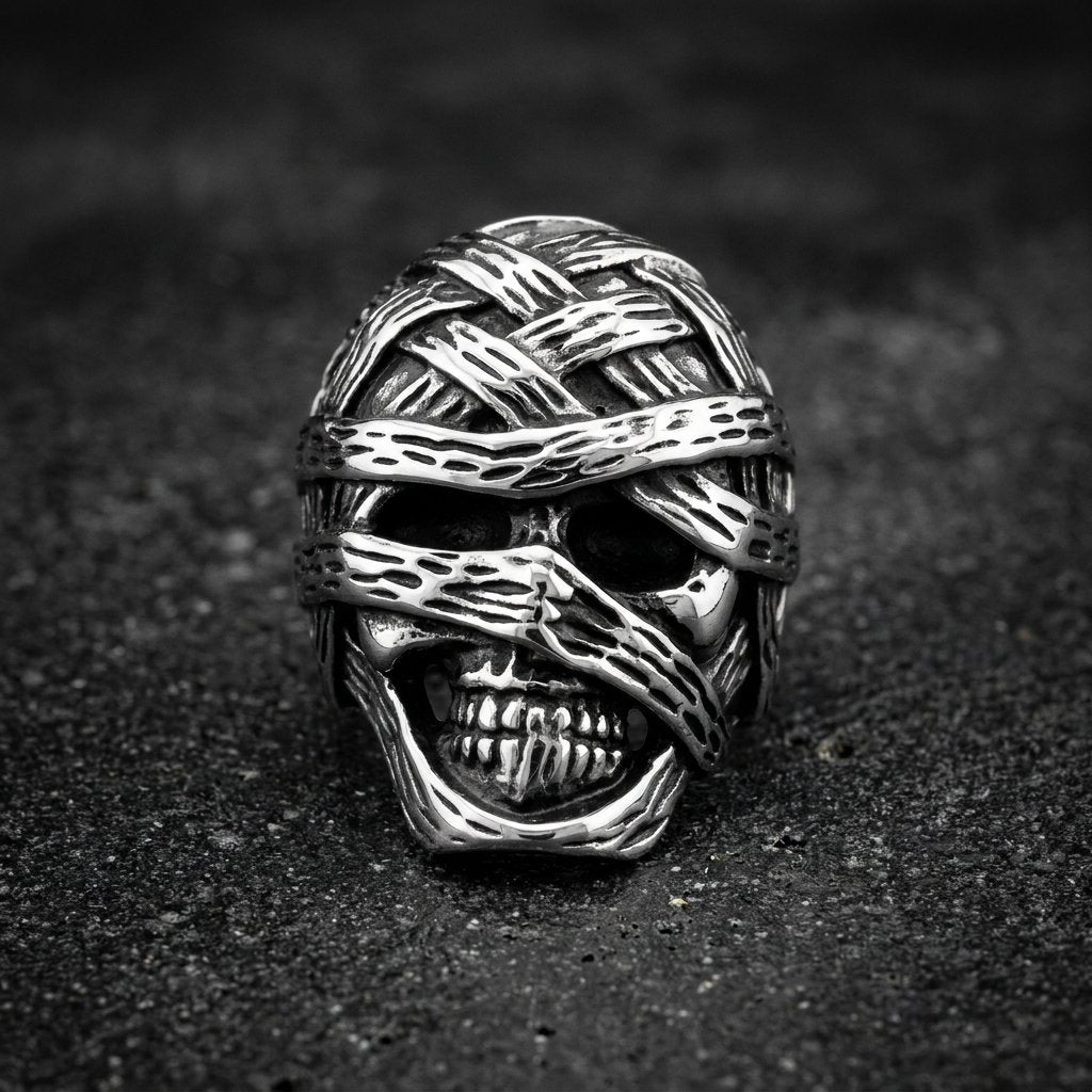 A silver-toned skull ring wrapped in textured bandages, photographed on a dark textured surface.