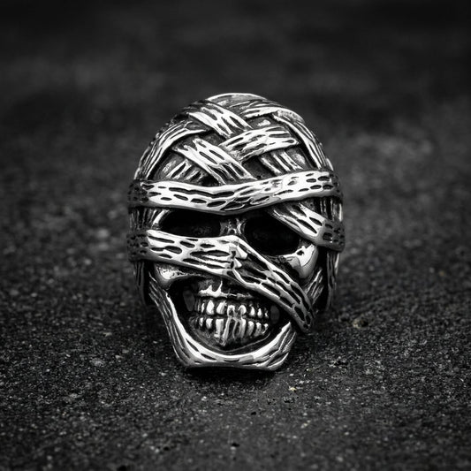 A silver-toned skull ring wrapped in textured bandages, photographed on a dark textured surface.