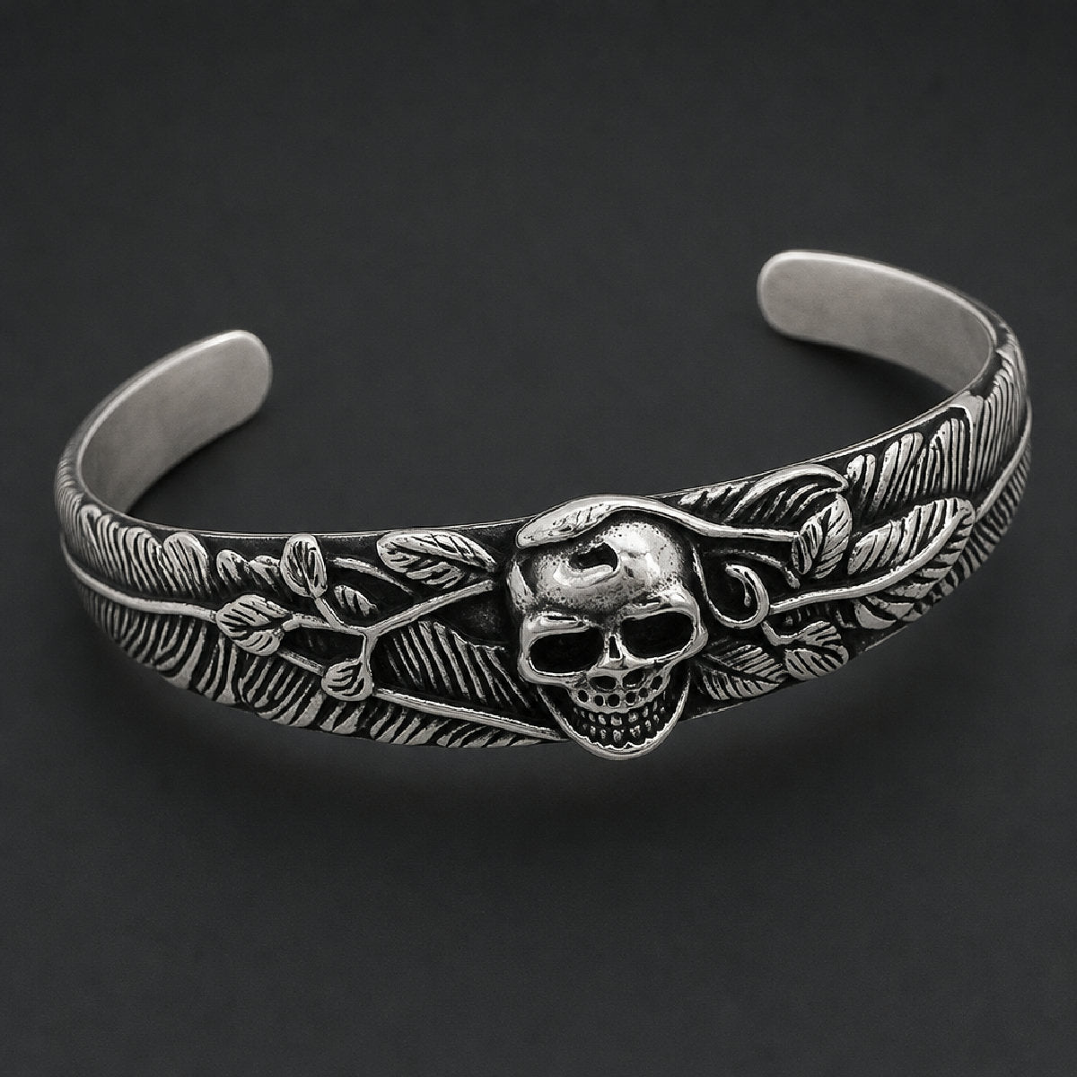 316L stainless steel open cuff bracelet featuring a detailed skull center surrounded by carved feather plumes and leaf accents in black and silver.