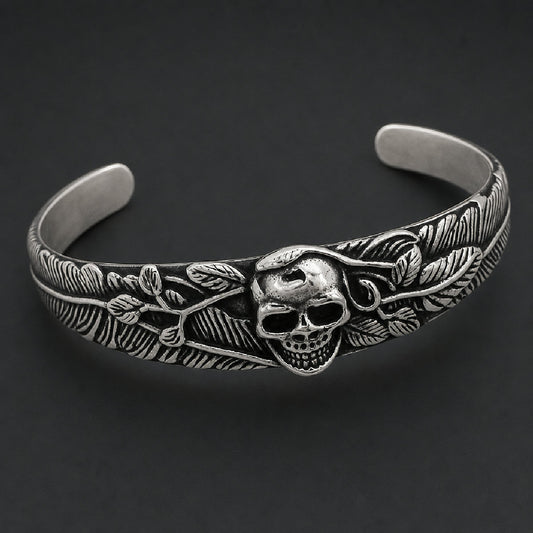 316L stainless steel open cuff bracelet featuring a detailed skull center surrounded by carved feather plumes and leaf accents in black and silver.