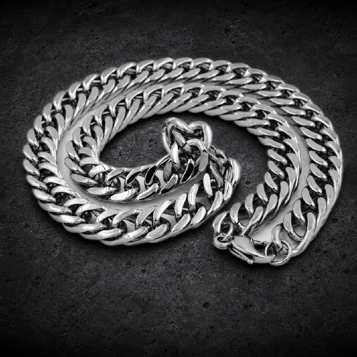 Highly polished 316L stainless steel curb chain necklace, featuring thick, flattened interlocking links. The chain is coiled on a white surface, showcasing its robust construction and shiny finish, with a lobster clasp visible at one end.