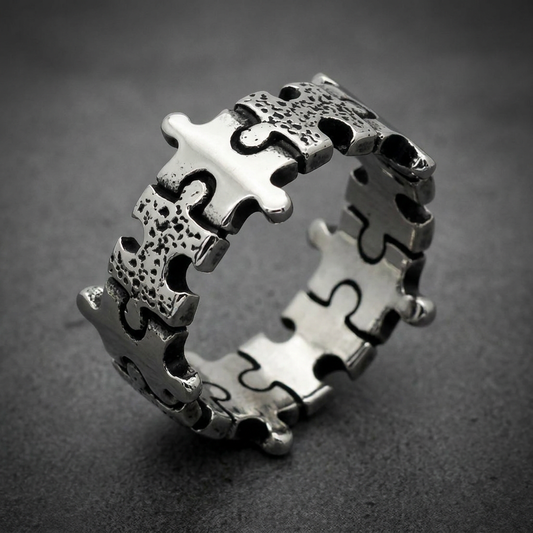 A wide, chunky unisex ring crafted from 316L surgical stainless steel, featuring interlocking puzzle piece motifs around the entire band. Some puzzle pieces have a smooth, polished finish, while others have a textured, granulated surface, creating a dynamic visual contrast. The ring has a solid-back HardKnocker construction, showcasing the natural bright silver tone of the steel.