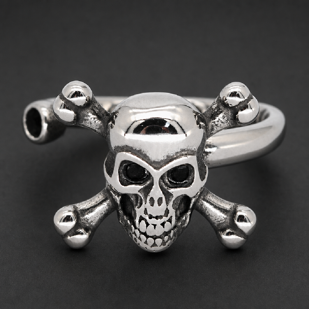 Shiny 316L surgical stainless steel unisex ring featuring a prominently detailed skull with black eye sockets and two crossbones behind it, set on a solid band with an antiqued finish in the recessed areas, showcasing a heavy and durable design.