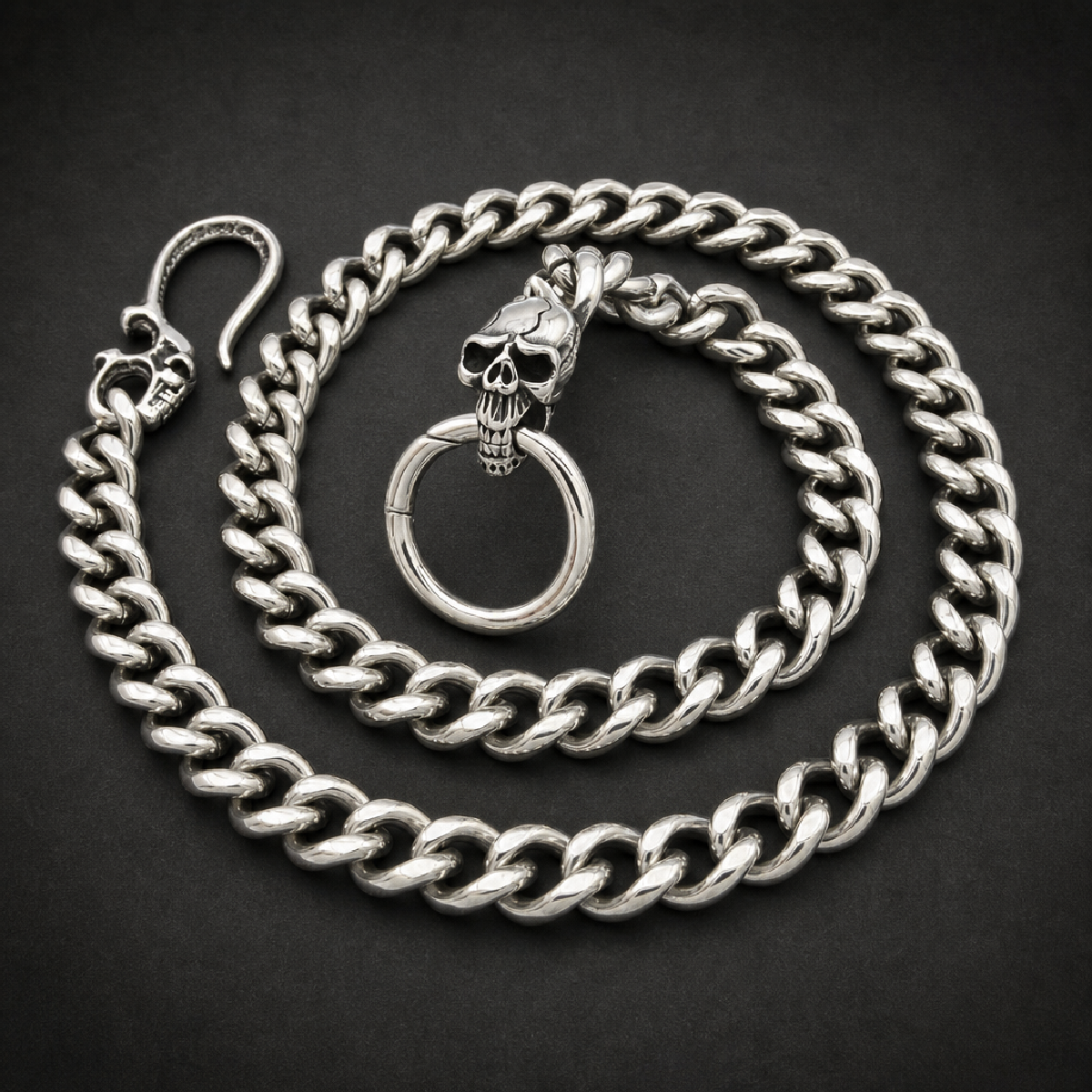 Heavy 316L stainless steel Cuban link wallet chain with two skull motifs, one on the spring gate ring attachment and one on the clasp, against a white background.