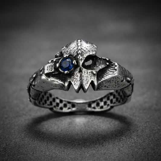 A rugged 316L stainless steel ring featuring a beast-like creature's jaw with sharp teeth and a single blue gemstone eye. The band has a scaly, textured finish, and the entire ring has an antiqued, dark silver appearance.