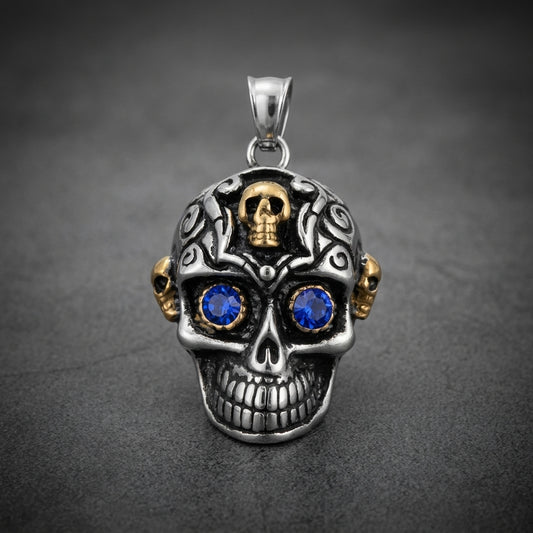 Prime Skull Pendant in 316L stainless steel with intricate dark engravings, two small gold skulls, and vibrant blue stone eyes.