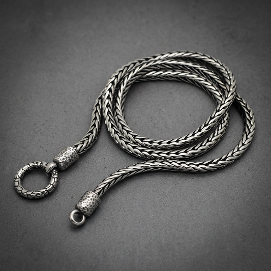 Silver 316L stainless steel Vaulted Chain Necklace with intricate woven links and detailed hammered end caps, coiled on a dark surface.
