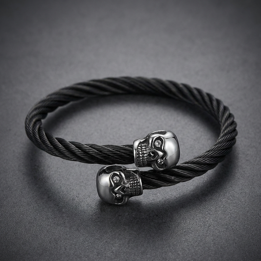 Black braided 316L stainless steel cable torque bracelet with two polished chrome-looking skull end pieces, one with a clear crystal eye.